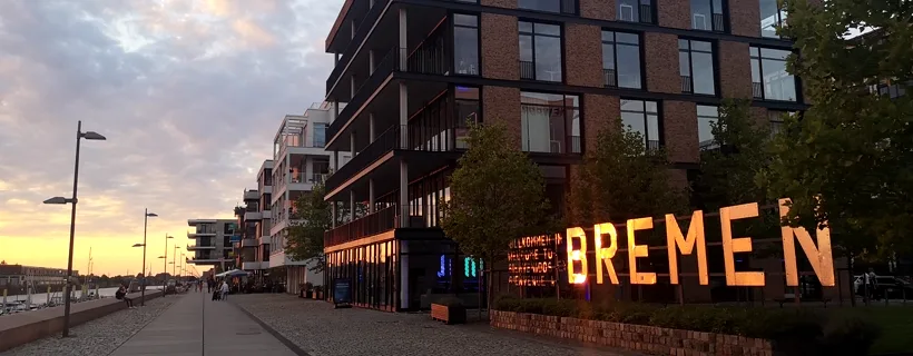 Die Bremer Überseestadt am Europahafen im Abendlicht, davor der beleuchtete BREMEN-Schriftzug